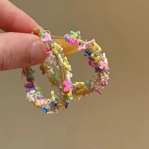 Détail de créoles dorées avec des papillons en résine colorés et des cristaux brillants