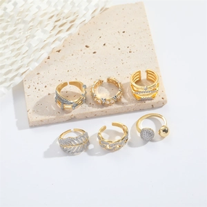 Set of six gold-plated leaf rings and zircon bands displayed on beige travertine stone