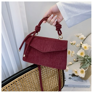 Close-up of wine red suede bag featuring a unique knotted handle and gold metal hardware