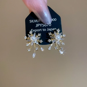 Detailed shot of golden snowflake earrings with sparkling zircons and a white pearl