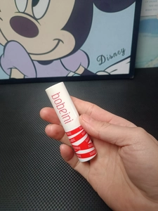 Close-up of matte lip mud tube with white body and red branding held by a hand