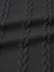 Close-up of black cable knit sweater fabric showing detailed weave texture and patterns