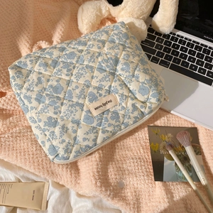 Quilted floral makeup bag shown on a pink rug with beauty accessories and a laptop