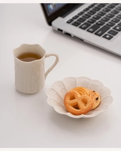 Macro detail of ceramic cup with bamboo relief design and petal-shaped saucer on a desk