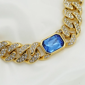 Dettaglio del bracciale a catena cubana dorata con gemma blu e cristalli chiari