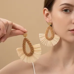 Détail de boucles d'oreilles en rotin tressé avec pompons boho et clou doré