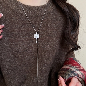 Detail view of a long silver necklace featuring a white flower pendant and pearl tassels
