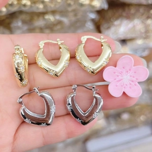 Detail of heart-shaped gold and silver earrings with intricate relief floral engravings