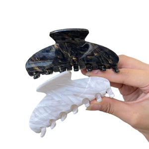 Handheld view of acetate hair claws in black gold and white pearl feather textures