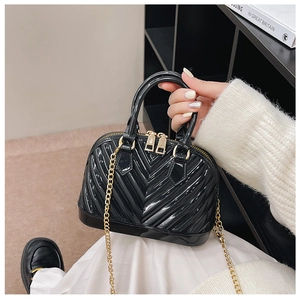Detail of black patent leather shell bag with V-quilt pattern and gold chain strap