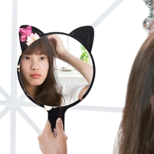 Handheld vanity mirror with black cat ear frame and pink floral pattern used by a model