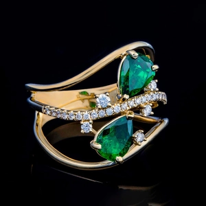Detalle macro de un anillo de gota dorado con piedras verde esmeralda y detalles de diamantes