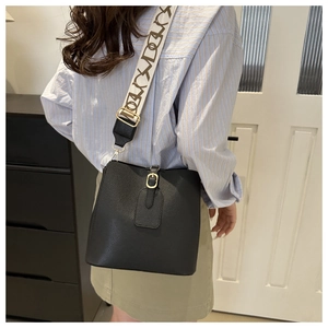 Detail of black pebbled leather bucket bag with wide geometric patterned shoulder strap