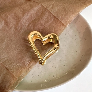 Close-up of a hollow heart-shaped metal hair claw clip with a polished gold finish