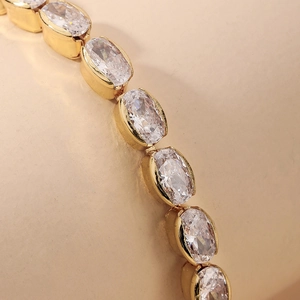 Detailed close-up of golden geometric bracelet with oval clear zircon stones and bezel setting