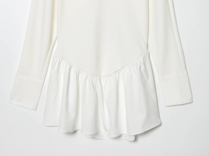 Close-up of white batwing sleeve dress with elegant ruffled hem and woven fabric detail