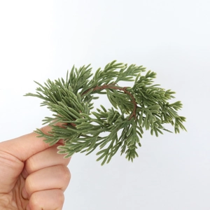 Close-up of hand holding a mini green PE pine needle wreath for festive table decor