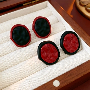 Détail des boucles d'oreilles géométriques rouge et noir avec texture rocheuse en boîte