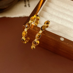 Dettaglio di orecchini vintage dorati con pietre occhio di tigre e piccoli zirconi bianchi