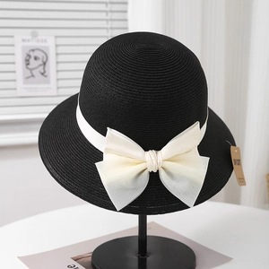Détail d'un chapeau de paille Hepburn avec grand nœud en satin et étiquette anti-UV