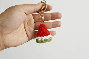 Macro detail of a handmade crochet watermelon keychain with gold metal lobster clasp