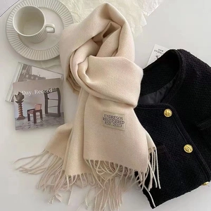 Beige solid color cashmere-like scarf with fringe and label, stylishly flat-layed on a white background