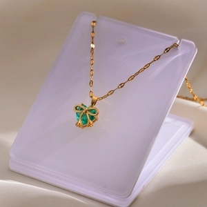 Close-up of gold plated necklace with green heart gemstone and dainty bow detail