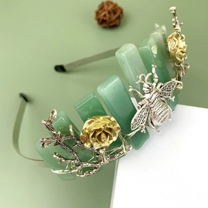 Detail of crystal crown with green flat stones, metal bees, and floral branches decor