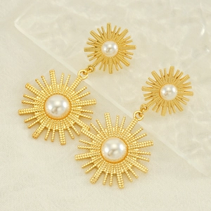 Detail of gold sunburst drop earrings with white pearls on a textured background
