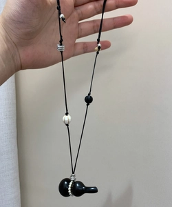 Detail of vintage wax cord necklace featuring black gourd pendant and pearl accents