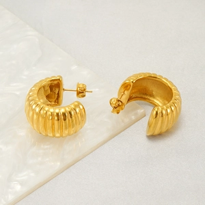 Close-up of golden C-shaped ribbed earrings on a white marble display background