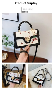 Detail of white leather handbag with red cherry print and twisted black handle and lock