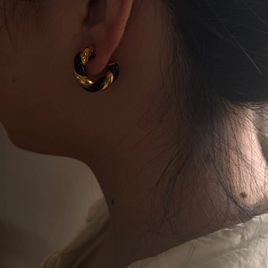 Detail of twisted gold and black enamel hoop earring worn by a model in French retro style