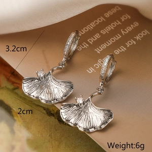 Detail of silver ginkgo leaf earrings with shimmering zircons on elegant satin