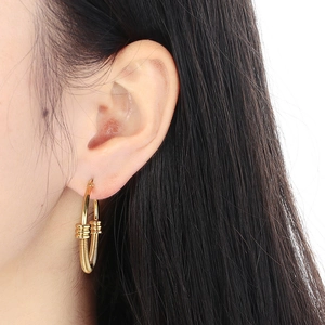 Gros plan de boucles d'oreilles créoles dorées avec texture torsadée sur l'oreille