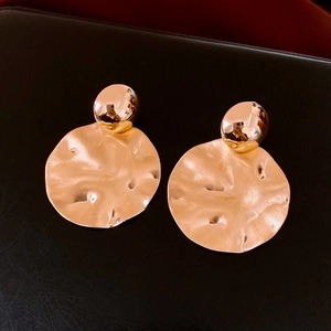 Detail of large gold hammered disc earrings with polished spheres on black leather surface