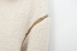 Détail du tissu polaire sherpa blanc avec liseré en daim marron sur le bord de la veste
