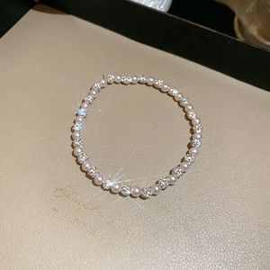 Macro detail of elegant pearl bracelet with diamond-encrusted beads on a beige tray