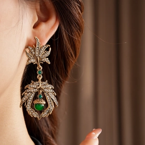Detail of vintage bronze leaf earrings with green gemstone and sparkling rhinestones