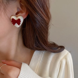 Close-up of heart-shaped earring with red velvet bow detail on model's ear