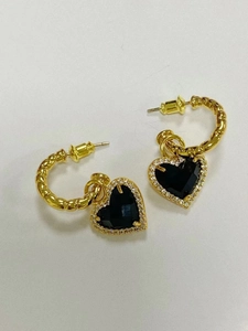 Dettaglio di orecchini a cerchio dorati con texture bambù e ciondoli a cuore nero