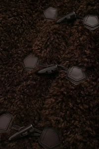 Macro view of dark brown faux fur texture with classic toggle button and leather patch