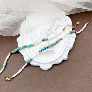 Detail view of handmade beaded bracelet with white beads and natural stones on a tray