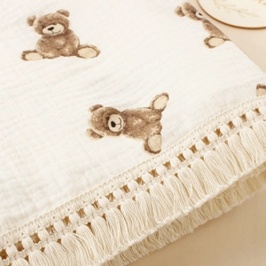 Detail of soft cotton muslin baby blanket with teddy bear print and fringe trim edges