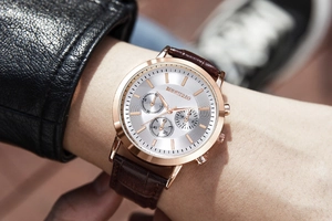 Close-up of a men's quartz watch with a rose gold case and brown leather strap on wrist