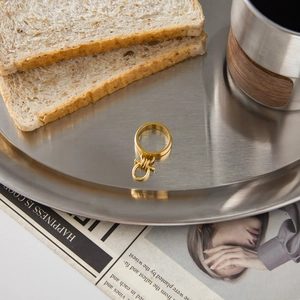 Detailed view of a gold Gancini style ring placed on a tray with lifestyle props