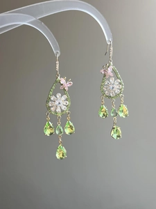 Macro detail of gold earrings featuring zircon butterflies and green teardrop pendants