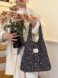 Floral black tote bag with pink flower pattern and central label carried by a woman