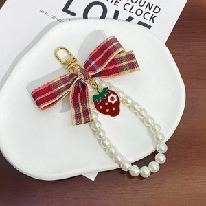Detail of red plaid bow keychain with strawberry pendant and pearl chain on ceramic plate