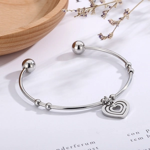 Detail of silver stainless steel open bangle featuring triple hollow heart charms and beads